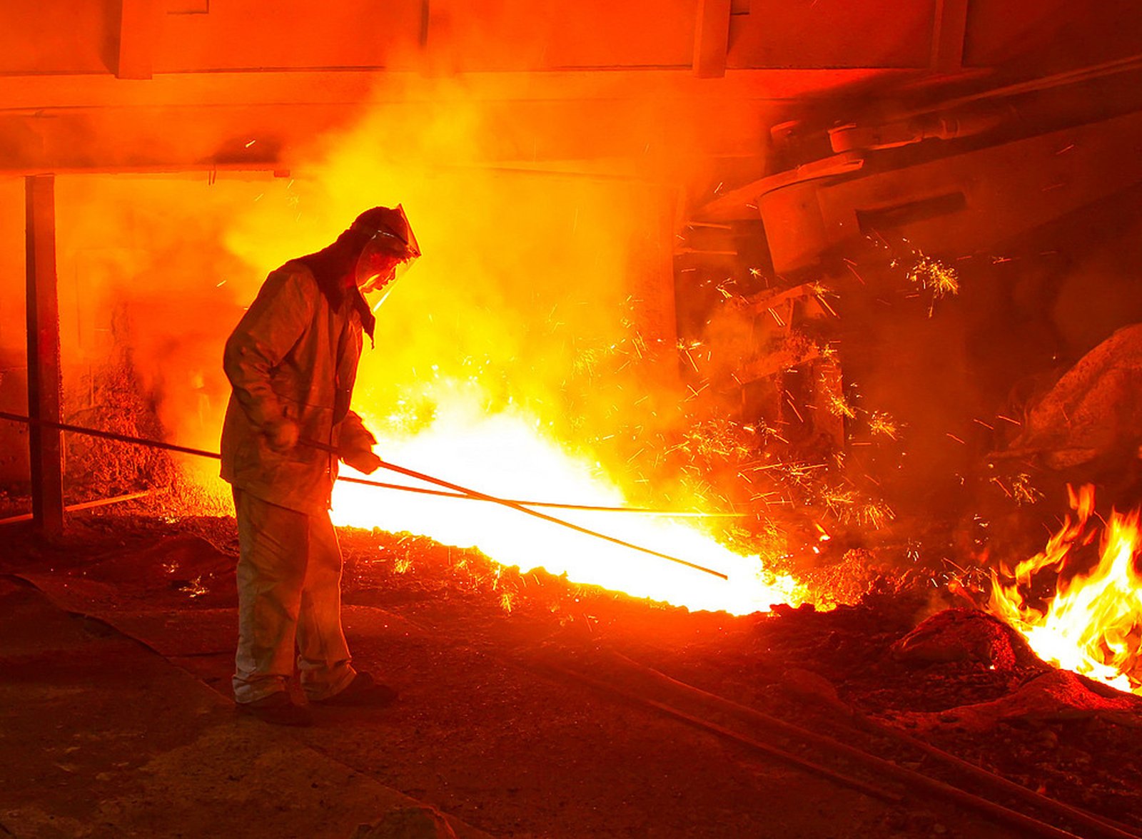 Industrial worker stirring glowing molten metal