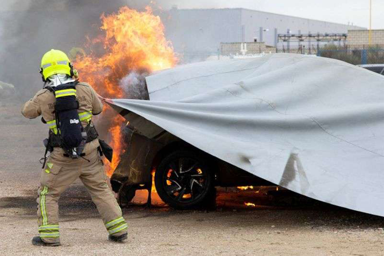 Firefighter smothering car fire with blanket